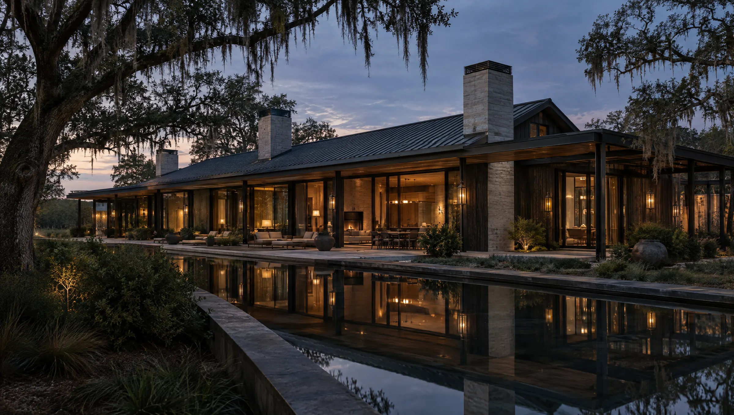 The Houston Estate clubhouse at dusk: charred cedar, stone and glass behind a still reflecting pool, under live oaks.