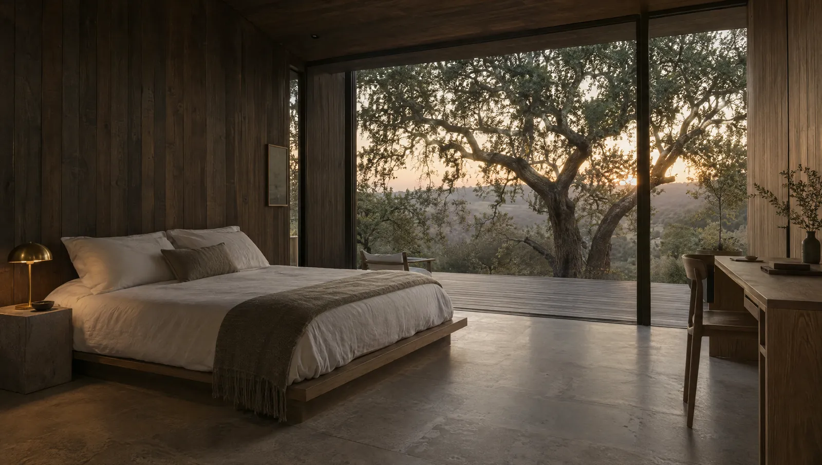 Inside a tiny guest home: a low platform bed, charred cedar walls and a wall of glass opening onto live oaks at dawn.