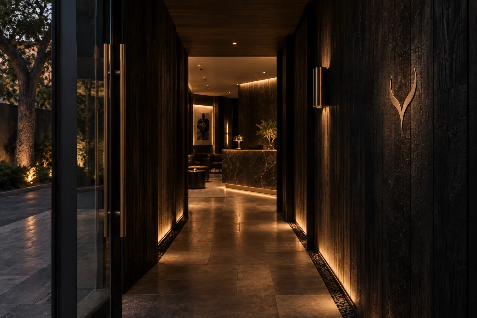 A dark charred-timber corridor lit low with brass, a brushed horn mark on the wall, and the reception glowing at the end.