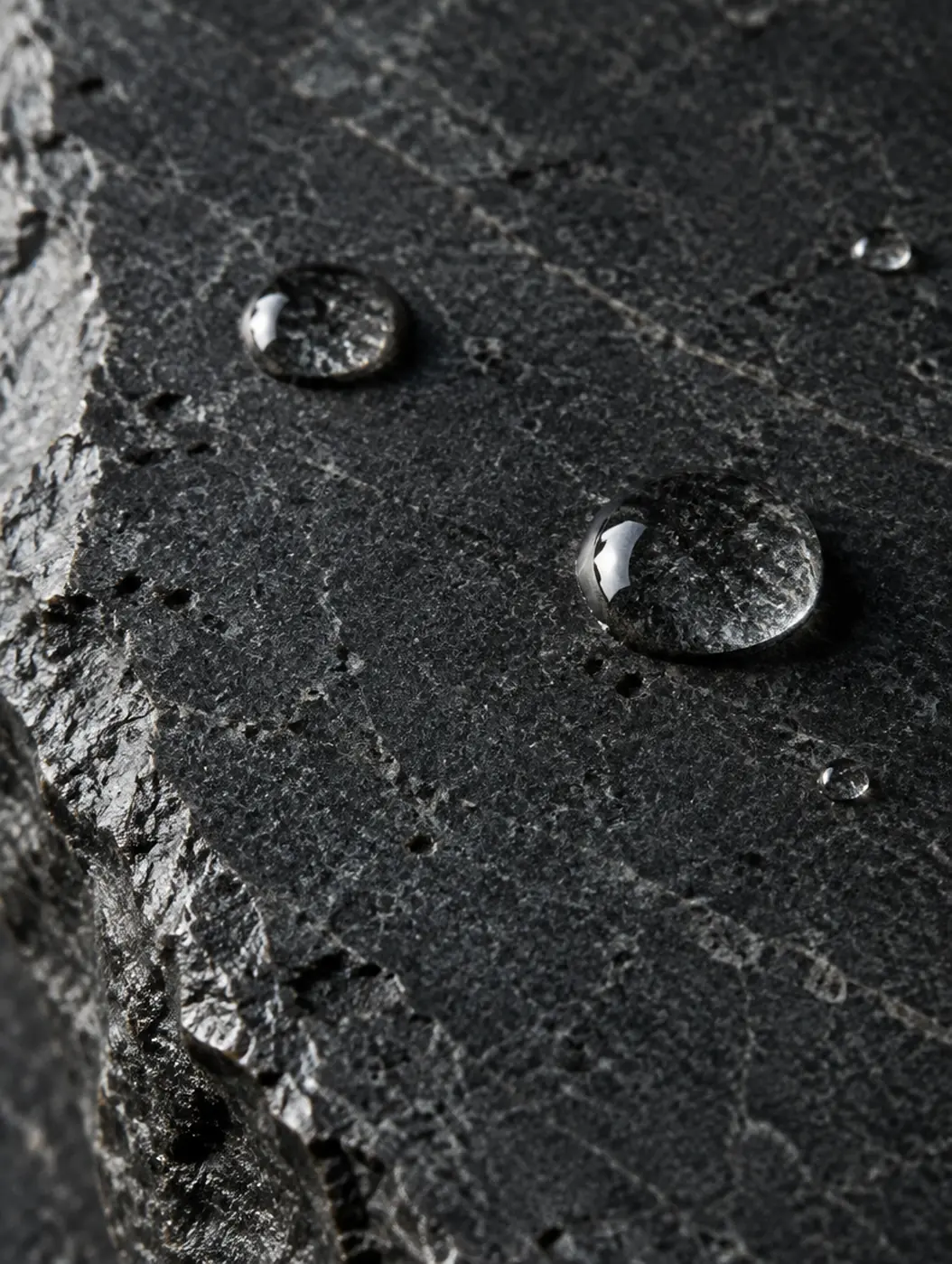 Dark honed stone with beads of water.