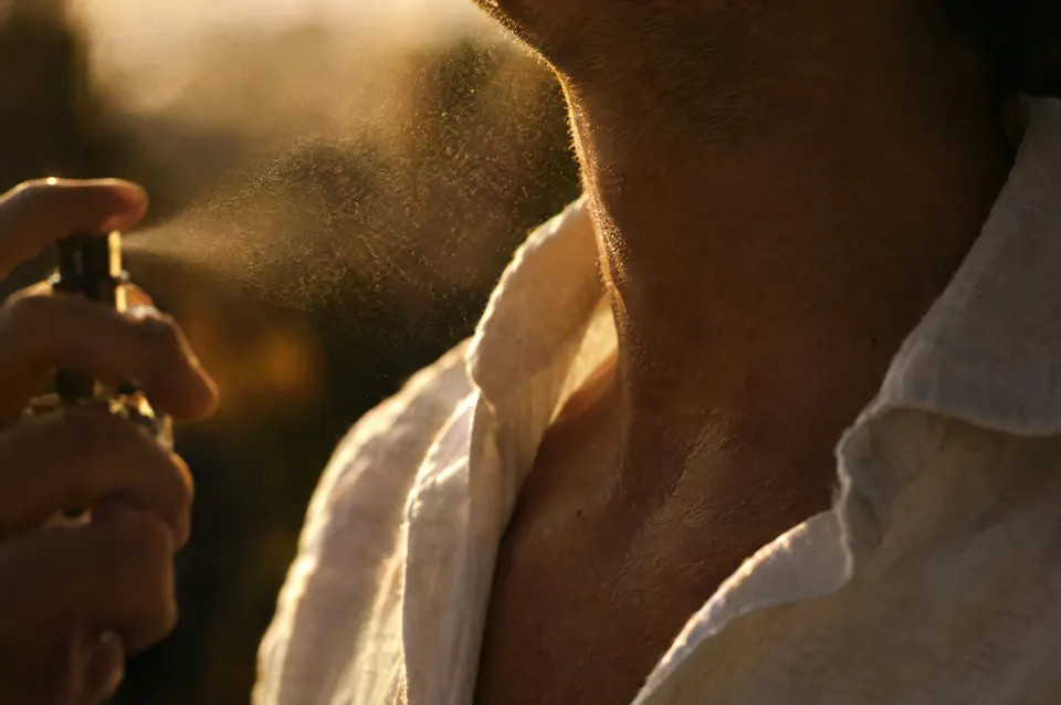 Close crop of a man’s neck and open collar as a fragrance mist settles, warm light on the skin.