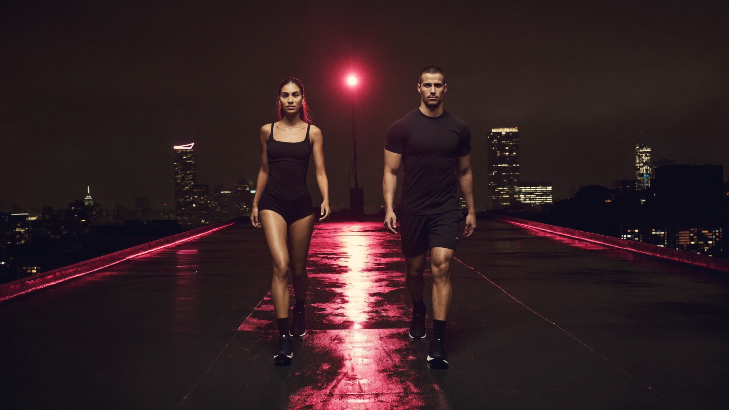 Two athletes stretching on a rooftop above a city skyline at night